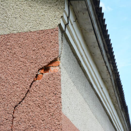 A serious stucco crack on the corner of the house near the rooftop. Repairing a stucco crack on the house wall.